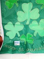 Close-up photo of the flag showing shamrocks and the gold embroidered text 'Happy St. Patrick's Day' on green fabric.