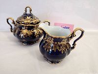 Front angle showing the sugar bowl with lid and creamer side by side, highlighting cobalt blue and gold patterns.