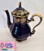 Front angle view of the cobalt blue Lindner Echt teapot with ornate gold decorations and a lidded top.