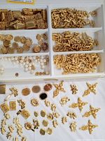 Assorted vintage gold-tone jewelry making components including setting bases, pendants, charms, and pearl-like beads arranged in trays and on fabric surface.