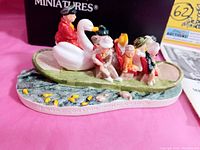 Side view showing swan boat with six seated figures, painted water base with fish, and inscribed base text.