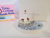 Signed miniature figurine of Boston Lighthouse on rocky coast with detailed water and buildings, original box and label visible.