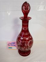 Full view photo of tall cranberry red glass decanter with matching stopper, showing its shape and cut to clear decoration.