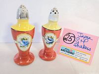 Pair of vintage Japanese lusterware salt and pepper shakers with floral blue rose design, metal tops, and yellow and red-orange ceramic bodies, marked JAPAN.
