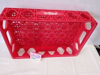 Red plastic Coca-Cola bottle tray, showing side view with handles and 'Enjoy Coca-Cola' logo.