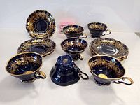 Complete set of six cobalt blue tea cups and matching saucers arranged on display, showing 24k gold detailing and design