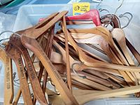 Close-up photo showing multiple vintage wooden hangers with metal hooks, some stamped with company names.