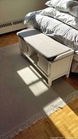 Full view of the white 3-section bed chest with cushioned padded top placed at foot of bed on beige area rug.