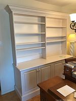 Front view of white two-piece wood buffet with hutch showing countertop and 4 cabinet doors below with 8 shelves above.