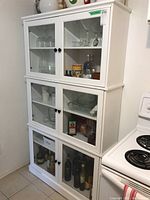 Front view of three stacked white MDF cabinets with beveled glass doors displaying glassware and bottles