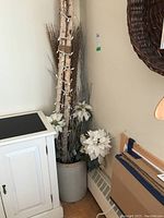 Wide shot of pottery crock filled with faux florals including white poinsettias, branches, and birch sticks with light string.