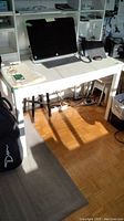 White Ikea style desk with computer and keyboard on top, showing full desk in a room with parquet flooring and some sunlight.