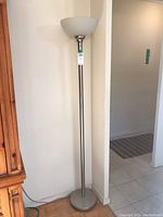 Full view of the torchiere floor lamp standing against a wall showing the entire lamp and base.