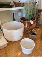 Wide shot showing the large milk glass meditation bowl alongside various planters including the large brown ceramic planter and the faux grass planter.
