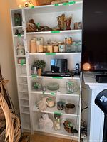 Two tall white shelving units placed side by side with various decorative items and dust on shelves.