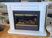 Front view of white Pyromaster electric fireplace with black and brass insert showing realistic logs and embers.