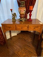 Front view of wooden console table with three small drawers and tapered legs.