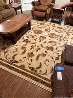 View of midsection and corner of beige floral patterned area rug on hardwood floor next to furniture.