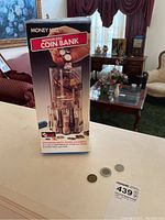 Original box of Money Mill motorized coin bank with three coins beside it.