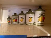 Full set of five ceramic canisters of varying sizes on shelf, decorated with fruit motifs.