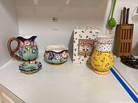Photo of all four ceramic pieces on shelf including ceramic pitcher, bowl, dish and boxed Mary Engelbreit vase.