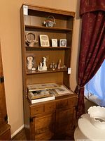 Front view of tall wooden Ethan Allen hutch and cabinet showing upper shelves with decorative items, three small drawers beneath, and a two-door cabinet at bottom.
