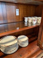 Photo showing stacks of plates in wood cabinet, including wash, dinner, and bread plates with red and green poinsettia pattern.