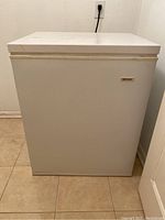 Front view of white Frigidaire chest freezer against wall, closed lid, powered off.