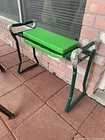 Photo of the green garden bench showing the full bench including cushioned seat and metal frame on a patio floor.