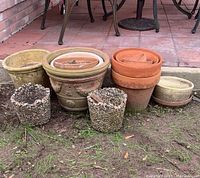 Photo showing 7 garden pots of various sizes and materials arranged on dirt and patio surface