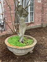 Full view of the large concrete statue of a woman carrying an urn, integrated within a concrete planter base outdoors.