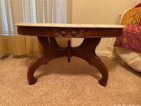 Side view of the oval wooden table showing carved floral details and curved legs.