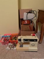 Singer 1744180 sewing machine with baskets of sewing accessories and boxes behind it, showing included items.