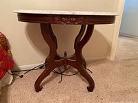 Front view of a marble top table with a carved wooden base showing floral detailing and curved legs.