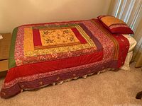 Bed setup showing colorful patchwork quilt and pillow on twin bed next to beige carpeted floor and window blinds
