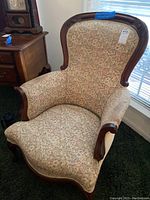 Photo showing full view of vintage high back upholstered chair with floral fabric and dark wood trimming at the top and sides.