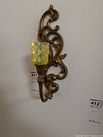 Wall sconce showing gold tone scroll design and textured yellow glass candleholder