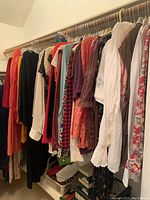 Wide view of assorted women's tops on hangers in various colors and styles, hung on a clothing rod above shoes and boxes.
