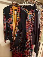 Black jacket or top with a vibrant multicolor plaid trim and matching plaid pants hung in closet on hangers.