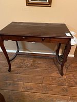 Front view of dark wood display table showing drawer and curved legs.
