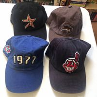 Four sports baseball caps displayed from front, showcasing different embroidered logos.