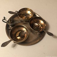 Tea set in assembled view on round tray with three bowls each containing a spoon, and decorative lamp figurine.