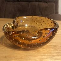Side angle photo showing amber art glass ashtray with bubble inclusions and curved cigarette rests on rim.