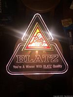 Front view of illuminated Blatz triangular bar sign lit up showing the logo and slogan glowing in dark environment.