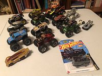 Top front angle showing majority of Hot Wheels toy vehicles including monster trucks, a gold futuristic car and a new silver race car in packaging.