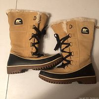 Full side view of both boots showing suede upper, fur lining, black laces and rubber lower half with SOREL patch visible.