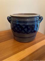 Blue salt glazed stoneware crock showing its body and one side handle, placed on a wooden surface