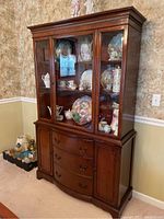 Full view of a dark hardwood breakfront china cabinet with glass display case on top and three drawers plus two cabinets below.