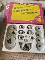 Photo of entire 17-piece child's Christmas tea set inside original box showing cups, saucers, plates, teapot, sugar bowl, and creamer with Christmas tree designs on each piece.
