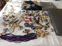 Wide view of a large assortment of assorted costume jewelry pieces with vintage bags and gloves on white cloth background.